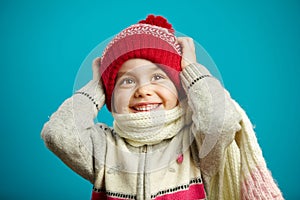 Surprised little girl in the christmas hat grabbed her head, expresses surprise and amazement, stands on blue background