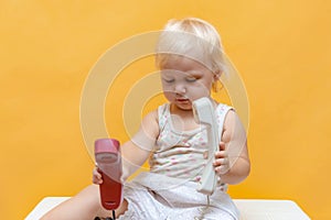 A surprised little girl holds a wired telephone receiver in her hands and does not know what to do with them
