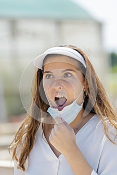 A surprised looking young woman pulling down her surgical mask. New lifestyle and safety concept