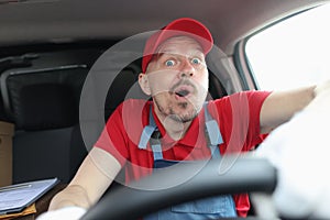 Surprised male courier in uniform is driving car