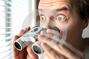 Surprised man with binoculars. Curious guy with big eyes. Nosy neighbour stalking or snooping secrets, gossip and rumour.