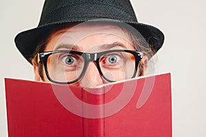 Surprised man in glasses looking out of the book. Nerd man has great ideas. Student reading an exciting book