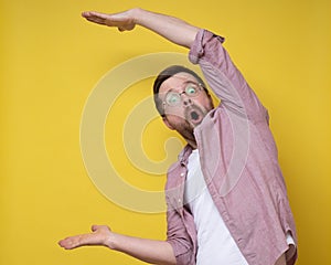 Surprised man in glasses shows a large size with hands, he exaggerates and looks at the camera in amazement. Copy space