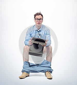 Surprised man in glasses, with tablet pc sitting on the toilet, on light background. Concept of situation