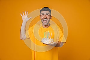 Surprised man holding birthday cake and screaming while standing isolated over yellow wall