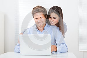 Surprised man looking at woman while using laptop