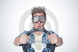 Surprised man in plaid shirt and stylish goggles with steering wheel, front view. Car driver concept