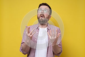 Surprised man raised his hands in supplication for a miracle and puzzled looks up.Yellow background.