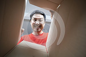 The surprised man unpacking, opening carton box and looking inside