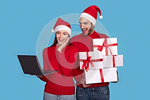 Surprised Man And Woman Wearing Santa Hats Holding Gift Boxes And Laptop