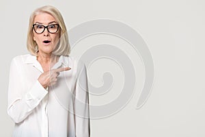 Surprised mature businesswoman pointing finger at copyspace isolated on background