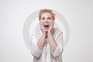 Surprised mature european woman shouting over gray background.