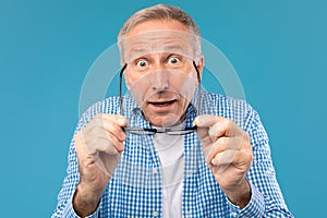 Surprised mature man taking off glasses staring at camera