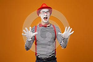 Surprised mime in red hat and striped t-shirt on blank orange background