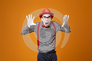 Surprised mime in red hat, white gloves and striped t-shirt on blank orange background