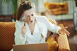 Surprised modern woman with laptop and magnifying glass