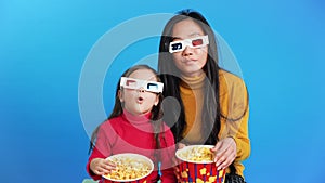 Surprised mother and her little daughter in 3D glasses with popcorn watching movie