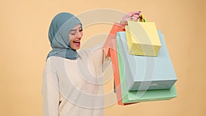 Surprised Muslim woman with shopping bags on beige background