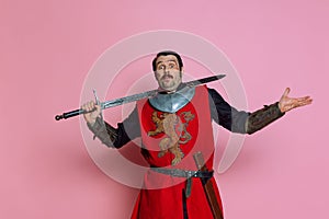 One young man, medieval warrior or knight wearing wearing armor clothing posing  over pink background