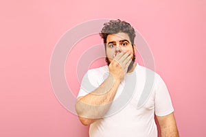 Surprised overweight guy stands on a pink background, closes his mouth in astonishment and looks into the camera. Fat funny curly
