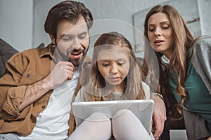 surprised parents and daughter looking at tablet