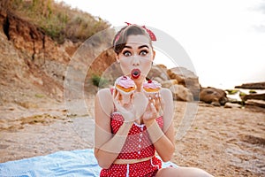 Surprised pin up girl showing two cream cakes sitting outdoors