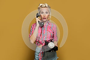 Surprised Pin-up woman holding retro phone posing on colorful yellow background