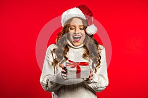 Surprised pretty woman smiling and holding gift box on red studio background.