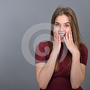 Surprised pretty young woman. Emotional beautiful girl over gray background.