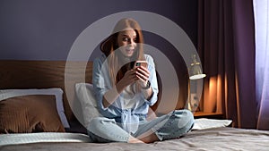 Surprised redhead young woman getting good online news on mobile phone at cozy bedroom.