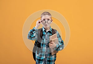 Surprised schooler with eyeglasses holding books on yellow background