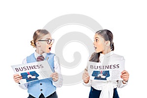 Surprised schoolgirls in formal wear with business newspapers looking at each other Isolated On White.