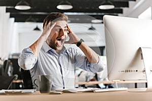 Surprised screaming business man using computer and holding his head