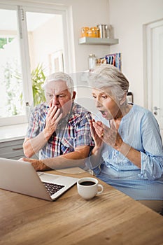 Surprised senior couple using laptop