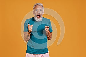 Surprised senior man pointing you and making a face while standing against orange background