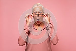 Surprised senior woman looking through glasses otices something unexpected