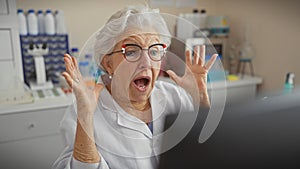 Surprised senior woman in white lab coat inside laboratory reacting to computer screen photo