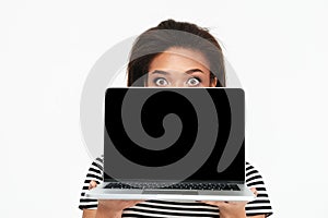 Surprised shocked african woman hiding behind blank screen laptop