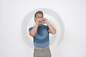 A surprised, shocked Asian man is talking on the phone with someone, isolated background