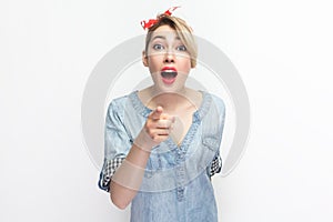 Surprised shocked blonde woman in red headband standing, pointing at you, looking with big eyes.