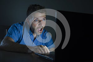 Surprised and shocked man at night working with laptop computer in the dark in disbelief and surprise face expression watching