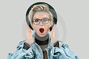 Surprised and shocked woman with opened mouth standing with open palms on gray background