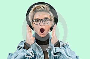 Surprised and shocked woman with opened mouth standing with open palms on green background