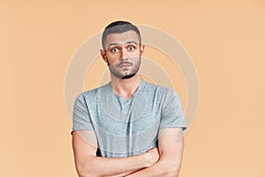 Surprised and shocked young man with crossed arms looking to camera over beige background