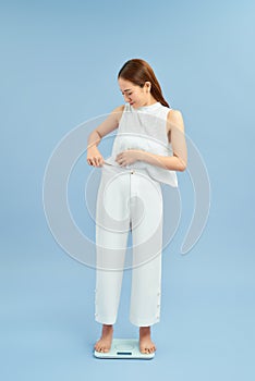 Surprised slim woman with scales on blue background. Weight loss concept