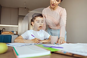 Surprised small teen boy looking with big eyes when mother showing mistake in homework.