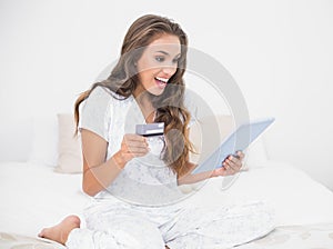 Surprised smiling brunette looking at tablet and holding credit card
