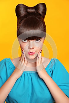 Surprised smiling teen girl with bow hairstyle, makeup and colourful manicured nails. Funny brunette in blue dress showing