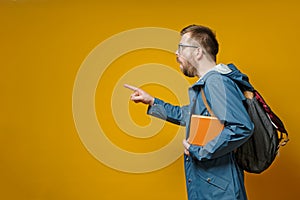 Surprised student with a book in hands in a stupor, he is puzzled and points with forefinger to the side with copy space