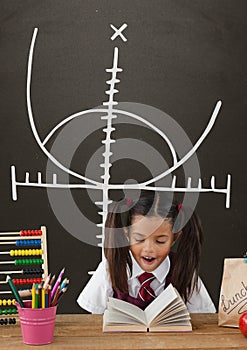 Surprised student girl at table against grey blackboard with education and school graphic